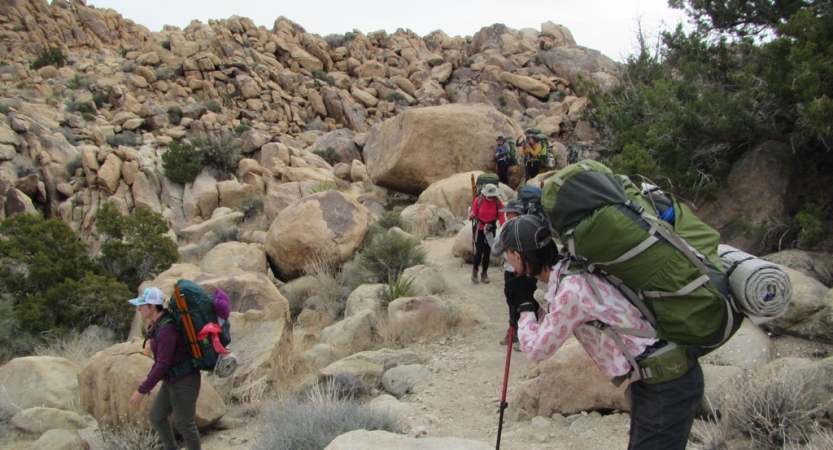 A group of veterans backpacking in joshua tree take a break among large rock formations.